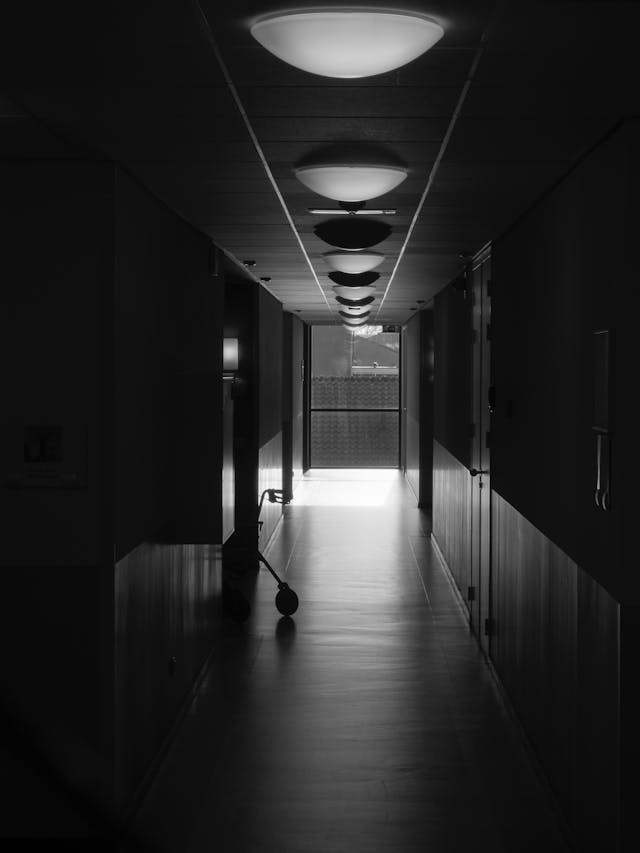Zdjęcie czarno-białe korytarza szpitalnego z widocznym wózkiem inwalidzkim