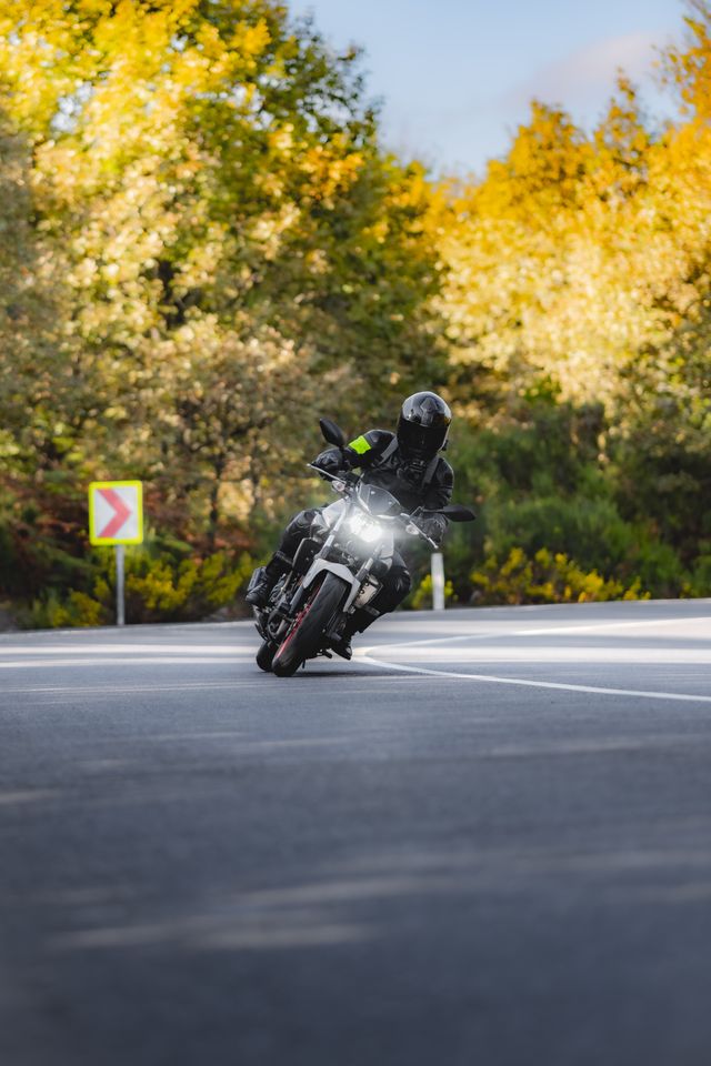 Zdjęcie motocyklisty na zakręcie z odblaskiem i na tle odblaskowego oznaczenia zakrętu